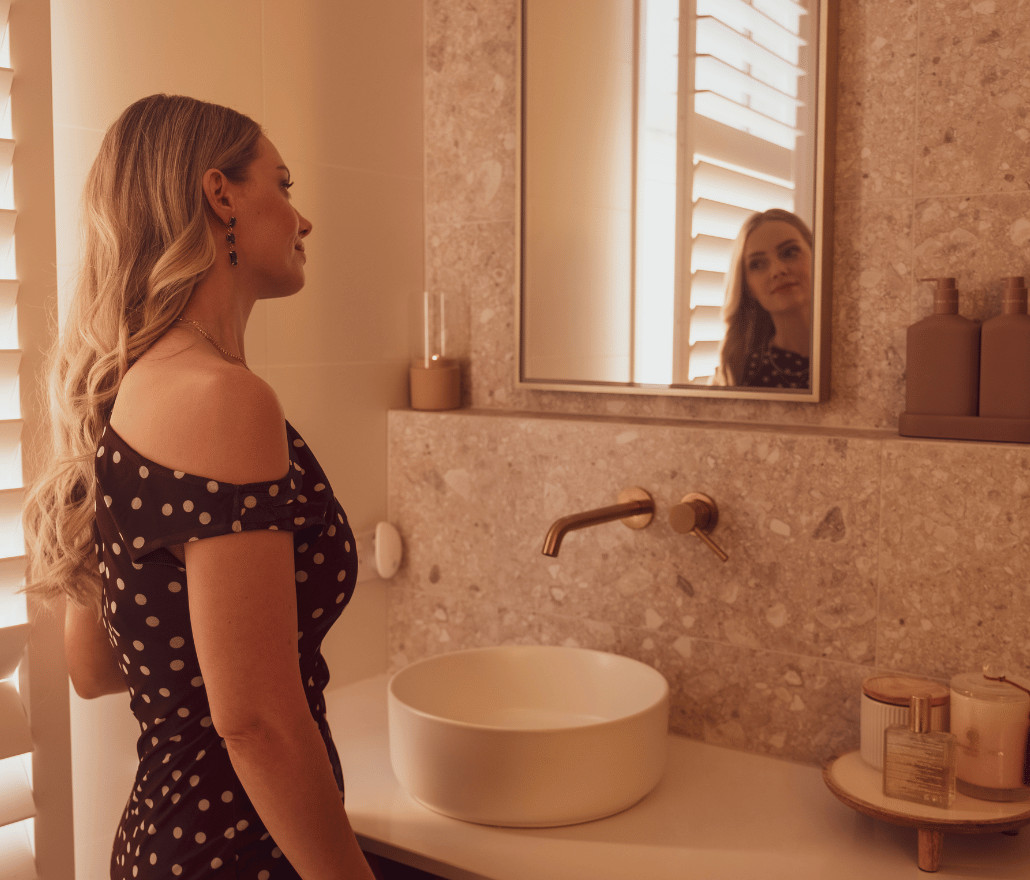 Woman at a bathroom vanity with a stone basin and brass tapware