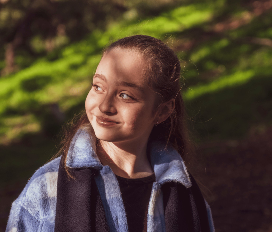 Girl in a blue coat standing among trees