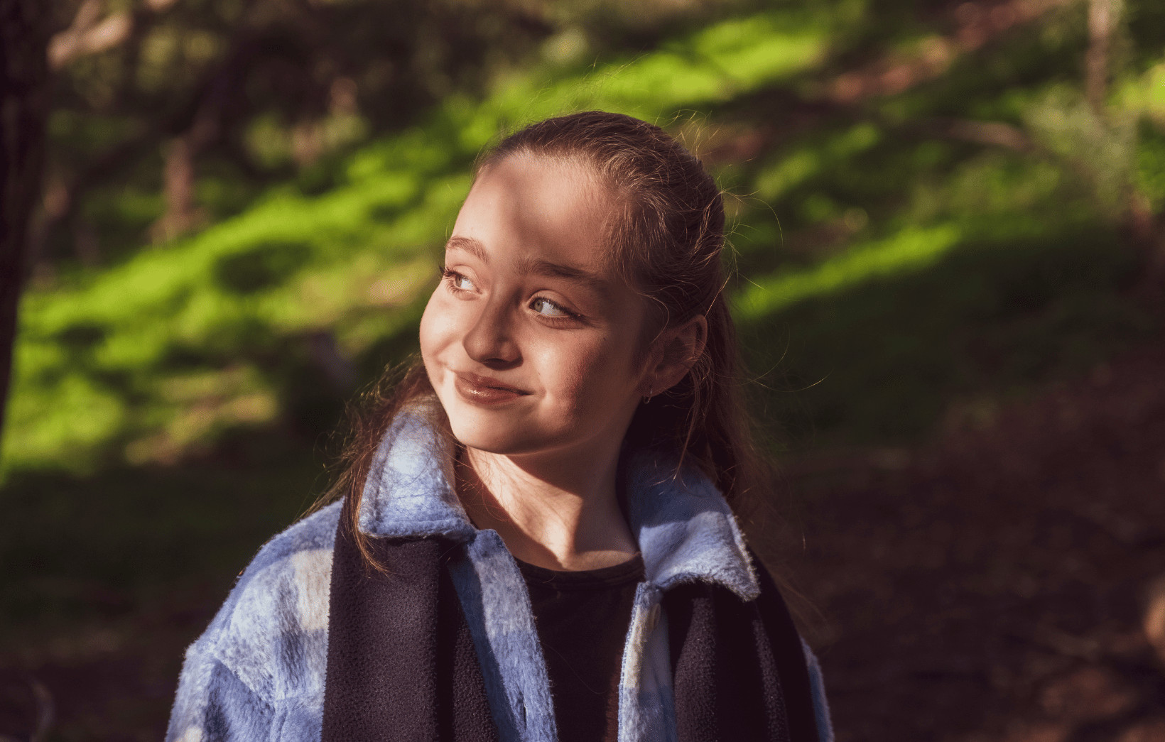 Girl in a blue coat standing among trees