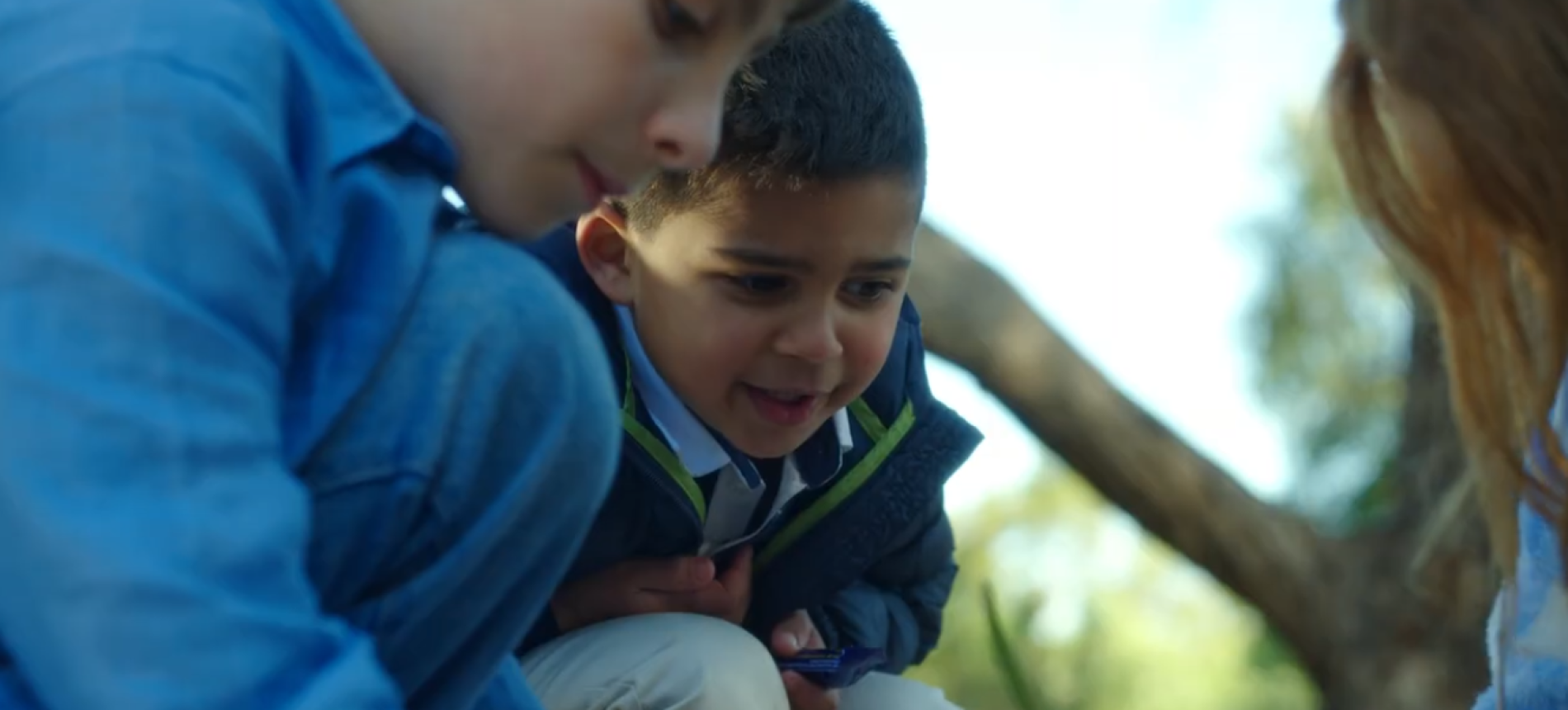 Three children crouched together looking at something outdoors